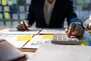 Close Up Of Businessman Or Accountant Hand Holding Pen Working On Calculator To Calculate Business Data, Accountancy Document And Laptop Computer At Office, Business Concept